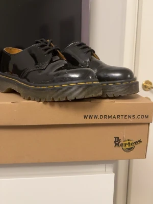 Svarta skor från Dr. Martens - Säljer ett par svarta loafers från Dr. Martens i glansigt lackläder. Insidan är ljusbrun med Dr. Martens-logga. Fick i present men har bara använt 2-3 gånger. De är köpta helt nya på scorett och har legat i lådan de kom i sen dess. 