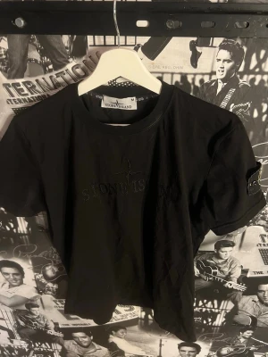 Svart Stone Island t-shirt - Snygg svart t-shirt från Stone Island med broderad logga på bröstet och klassisk patch på ärmen. T-shirten har rund hals och är tillverkad i mjuk bomull. Perfekt för en stilren och trendig look.