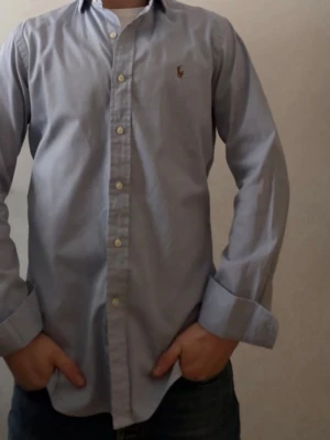 Ljusblå skjorta från Polo Ralph Lauren - Klassisk ljusblå skjorta från Polo Ralph Lauren i slim fit-modell. Skjortan har långa ärmar, knappar framtill och den ikoniska broderade loggan på bröstet. Tillverkad i mjuk bomull för en skön känsla och stilren look. Skick 9/10✅ 