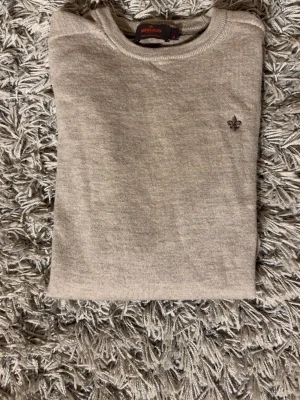 Beige tröja från Morris - Snygg beige tröja från Morris med diskret broderad logga på bröstet. Tröjan har rund halsringning och är tillverkad i ett mjukt, tunt stickat material som känns skönt mot huden. Perfekt för lager på lager och enkel att matcha. S passar M