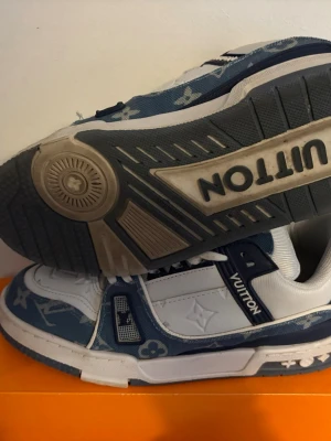  blåvita sneakers - Snygga sneakers i blått och vitt med klassiskt monogrammönster på denimdetaljer. Skorna har vita läderpartier, tydlig  på plösen och robust sula med -tryck undertill. Perfekta för dig som vill sticka ut med exklusiv streetstyle.