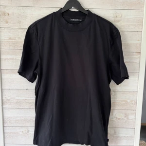 Svart t-shirt från J.Lindeberg - En stilren svart t-shirt från J.Lindeberg med klassisk rund halsringning. T-shirten har normal passform, perfekt för en clean och enkel look.