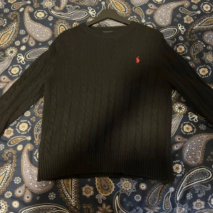 Svart stickad tröja från Polo Ralph Lauren - stickad svart tröja från Polo Ralph Lauren. Den är ungefär 8 månader gammal men knappt använd, den har inga skador eller fläckar, säljer den biligt eftersom jag har slängt orginal påse/tag och kvitto, kontakt mig cid intresse!