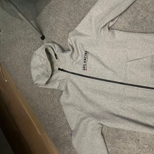 Grå hoodie från Sail Racing - Säljer en fin sailracing hoodie. Tröjan är i jätte fint skick. Säljer på grund av att den är lite förstor.