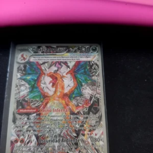 Charizard VMAX Pokémonkort - Säljer ett Charizard VMAX Pokémonkort med färgstark illustration av Charizard och holografiska detaljer. Kortet har text på spanska och visar 330 HP. Perfekt för samlare eller Pokémon-fans!