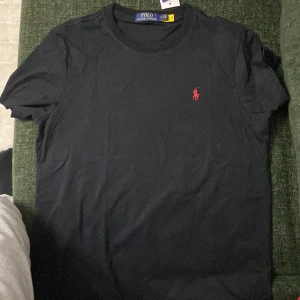 Svart och vit t-shirt från Polo Ralph Lauren - Två klassiska t-shirts från Polo Ralph Lauren, en svart med röd broderad logga och en vit med blå broderad logga. Båda har rund hals och korta ärmar. Perfekta för en stilren och enkel look.