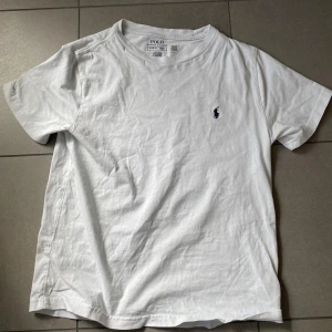 Vit t-shirt från Polo Ralph Lauren - Vit t-shirt från Polo Ralph Lauren, som är köpt i Spanien på en resa. Denna T-Shirt har en broderad marinblå logga på bröstet. Denna är inte så använd, en vad jag trodde när jag köpte den. T-shirten har rund hals och korta ärmar, tillverkad i mjuk bomull för en skön känsla.