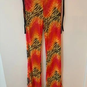 Assnygga mönstrade byxor från I.AM.GIA❤️🧡💛 - Snygga byxor från I.AM.GIA med djurmönster i orange, rött och gult. Byxorna har dragkedja bak  och dragsko på sidorna. Använda men i fint skick. 