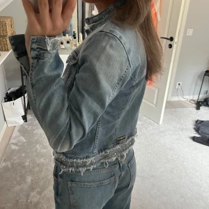 Ljusblå jeansjacka - Säljer en snygg ljusblå jeansjacka med fransdetaljer och slitningar längs nederkanten och ärmarna. Lite osäker på märket, sista bilden tog jag bild på märket. Det står att jackan är en L, men skulle uppskatta den som en S