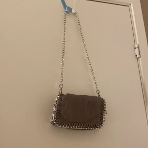 Beige axelväska med kedjedetaljer - Säljer en beige axelväska med grov silverkedja som axelrem och runt kanterna. Väskan är i skinnimitation med en cool, lite ruffad struktur. Perfekt storlek. Har lite hål vid mangneten, så pris kan diskuteras 💕