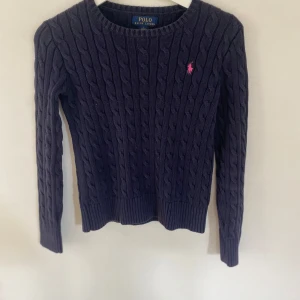 Mörkblå kabelstickad tröja från Polo Ralph Lauren - Säljer en mörkblå kabelstickad tröja från Polo Ralph Lauren med rund halsringning och rosa broderad logga på bröstet. Tröjan ör i fint skick. Storlek L barn men passar perfekt som xs dam. Pris kan diskuteras. 