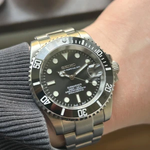 Seikomod Submariner 40mm - Stilren Seiko Submariner-inspirerad klocka med svart urtavla, datumvisning och vridbar bezel. Boett och länk i silverfärgat rostfritt stål. Klassisk design med tydliga index och robust känsla. Inuti sitter ett Nh35 urverk från Seiko. Klockan är vattentät och har lume på visarna som gör det lättare att läsa tiden i mörkret. Skicka dm vid frågor eller prisförslag 😁📩