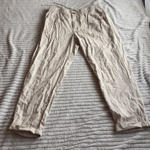 Beige linnebyxor från H&M - Säljer ett par beige linnebyxor från H&M med regular fit och elastisk midja med dragsko. Byxorna har raka ben och är tillverkade i ett lätt och luftigt linnematerial, perfekta för varmare dagar.