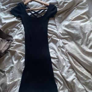Svart ribbad kortklänning från Bershka - Svart ribbad kortklänning från Bershka med snygga korsade band i ryggen. Klänningen har korta ärmar och en tight passform som framhäver figuren. Den är väldigt väldigt stretchig och skön!!