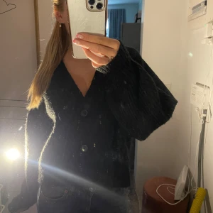 Stickad kofta - Mysig svart stickad kofta med v-ringning och stora knappar framtill. Koftan har långa, lite pösiga ärmar och en loose passform .