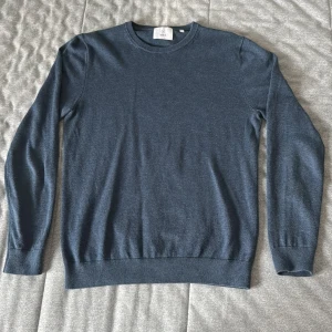 Blå stickad tröja från Bläck - Mörkblå stickad tröja från Bläck i storlek S. Klassisk rund halsringning och ribbade muddar vid ärmslut och nederkant. Perfekt för lager-på-lager och enkel att matcha med jeans eller chinos.