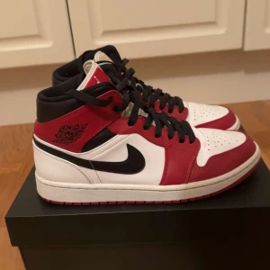 Nike Air Jordan 1 Chicago sneakers - Säljer ett par ikoniska Nike Air Jordan 1 Chicago i rött, vitt och svart skinn. Klassisk high-top siluett med svart swoosh, perforerad tå och svarta skosnören. Perfekta för dig som vill sticka ut med en tidlös sneakerlegend. Nypris är 2600kr