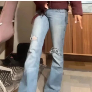 Ljusblå bootcut jeans med slitningar - Säljer ett par ljusblå jeans med bootcut passform och snygga slitningar på knäna. Jeansen har klassiska fickor både fram och bak, samt råa kanter nertill för en extra edge. Perfekta för dig som gillar en avslappnad och trendig stil.