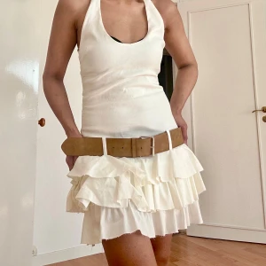 Vit volangkjol från Zara - Supersöt vit kortkjol från Zara med flera lager volanger som ger en riktigt flowy känsla. Kjolen har en snygg passform och är gjord i ett lätt bomullstyg, perfekt för varma dagar. Styla med bälte för extra edge!