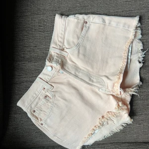 Persika färgade jeansshorts från Levi's - Snygga persikafärgade jeansshorts från Levi's med hög midja och fransiga kanter. Klassisk femficksmodell med knapp och dragkedja framtill. Perfekta för sommardagar när du vill ha en chill och trendig look.