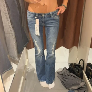 Blå bootcut jeans med slitningar - Snygga ljusblå bootcut jeans med slitna detaljer på framsidan och klassiska bakfickor med knapp. Låg midja och lätt utsvängda ben ger en retro vibe. Perfekta för dig som gillar en avslappnad men trendig look.