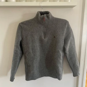 Grå halvzip ulltröja från Polo Ralph Lauren - Mysig grå stickad tröja från Polo Ralph Lauren med halv dragkedja och hög krage. Broderad röd logga på bröstet. Passar ej mig så därav säljes:)