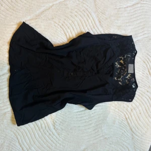 Svart blus med spets från Vero Moda - Supersnygg svart blus från Vero Moda i storlek XS. Blusen har v-ringning, knappar framtill och detaljer i spets över axlar och övre rygg. Perfekt för dig som gillar en stilren look med lite extra detaljer.