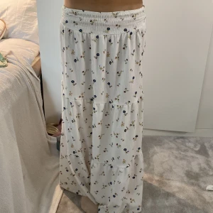 Vit blommig långkjol från lager 157, XS - Supersöt långkjol från 157 i vitt med små blommor i blått, rosa och grönt. Kjolen har smock i midjan och faller snyggt i flera volanger. Perfekt för vår och sommar när du vill ha en chill och härlig vinbe 