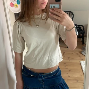Beige topp med puffärm Filippa K XS - Säljer en stilren beige topp från Filippa K i storlek XS. Toppen har puffiga korta ärmar och en lite högre halsringning. Den är gjord i mjuk bomull och har en croppad passform som känns modern och enkel att styla.