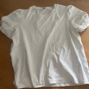 Vit t-shirt med puffärm från Indiska - Säljer en basic vit t-shirt från Indiska i storlek L. T-shirten har korta puffärmar och är gjord i mjuk bomull. Perfekt till jeans eller kjol för en clean och fräsch look.