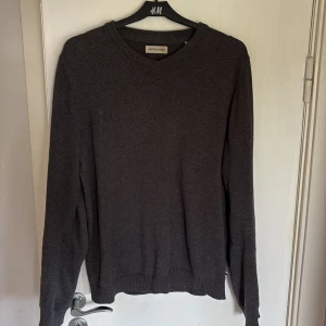Mörkgrå stickad tröja Jack & Jones - Mörkgrå stickad tröja från Jack & Jones i klassisk modell med v-ringad hals. Tröjan har ribbade muddar vid ärmslut och nederkant, och är långärmad. Perfekt för lager-på-lager och enkel att matcha med jeans eller chinos.