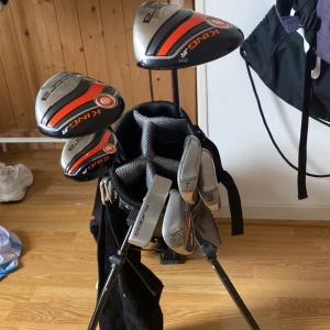 Cobra golfbag i svart och orange - Säljer en Cobra golfbag i svart och orange med flera fack och praktiska bärremmar. Väskan har tydliga loggor och detaljer i grått och orange. Perfekt för att bära golfklubbor och tillbehör på banan. 10-12 år