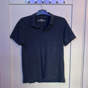 Mörkblå pikétröja Hampton Republic - Snygg mörkblå pikétröja från Hampton Republic i klassisk modell med krage och korta ärmar. Tröjan har diskret logga broderad på bröstet. Perfekt för en clean och stilren look.