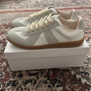 Maison Margiela sneakers vit/grå - Maison Margiela  sneakers i vitt och ljusgrått med beige snörning och klassisk gummisula. Skriv ett meddelande vid frågor eller funderingar. 