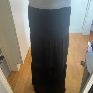 Svart långkjol🤍 - Svart långkjol med elastisk midja och broderade hål i blommönster. Kjolen har en lätt volang och är tillverkad i ett mjukt tyg som känns skönt mot huden. Perfekt för dig som gillar en stilren men ändå detaljrik look🫶🏻