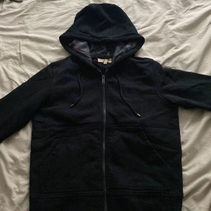 Svart hoodie från burberry - Svart hoodiejacka med hel dragkedja framtill och justerbar huva med snörning. Jackan har långa ärmar och två stora fickor framtill. Perfekt för lager-på-lager och chill vardagsstil.