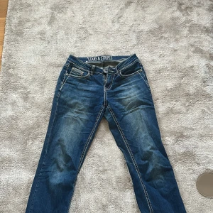 Blå jeans Stars & Stripes med broderi - Snygga blå jeans från Stars & Stripes med coola broderade bakfickor och kontrastsömmar. Jeansen har normal passform och klassisk femficksdesign. Perfekta för dig som vill sticka ut lite extra med detaljer på fickorna. Priset kan även diskuteras.