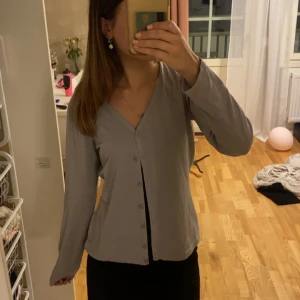 Glittrig silverkofta  - Supersnygg glittrig silverkofta från ExlindExlind med v-ringning och knappar framtill. Långärmad och i ett mjukt, stretchigt material som ger en riktigt cool look. Perfekt att styla till jeans eller kjol för en extra touch.