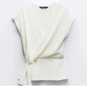 Vit omlottopp från Zara - Stilren vit omlottopp från Zara med knyt i sidan. Toppen har korta ärmar och en elegant v-ringning. Perfekt för dig som gillar minimalistisk och fräsch stil.