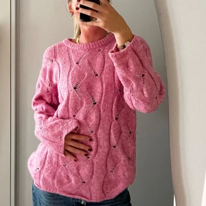 Rosa stickad tröja med vågigt mönster - Superfin rosa stickad tröja med vågigt hålmönster och rund hals. Tröjan har en loose passform och långa ärmar, perfekt för lager på lager.