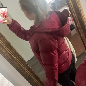 Röd pufferjacka med huva - Säljer en snygg röd glansig pufferjacka från Design by Amor. Jackan är använd 1-2 gånger och säljer på grund av för lite användning. Perfekt till vintern då den är varm och skön❣️