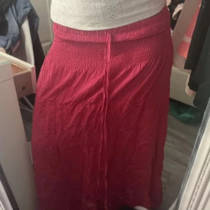 Rosa långkjol med resår och knyt - Snygg rosa långkjol med resår i midjan och knytband framtill. Kjolen är luftig och har en enkel, rak passform som gör den bekväm att bära. Perfekt för dig som gillar färg och vill ha en skön kjol till sommaren.