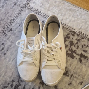 Vita sneakers från Gant, storlek 40 - Klassiska vita sneakers från Gant i canvas med snörning och rund tå. Snygg broderad Gant-logga på sidan och platt sula. Perfekta till jeans eller shorts för en clean och stilren look.