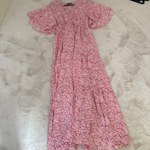 Blommig långklänning från SHEIN - Söt långklänning från SHEIN med rosa och röda blommor. Klänningen har v-ringning, korta volangärmar och ett luftigt fall. 