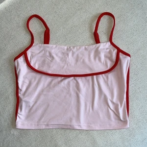 Rosa linne med röda kanter - Söt croppat linne i ljusrosa med röda kontrastkanter och smala justerbara axelband. Jättebra skick, endast använd fåtal gånger