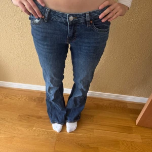 Blå låg midjade jeans med rosett-detalj från Monki - Snygga blå jeans från Monki med raka ben och coola fickor bak som har broderade rosetter och vita knappar. Klassisk femficksmodell med normal midja och skön passform. Perfekta för dig som vill ha något unikt i garderoben.  Midjemått: 38cm 💕