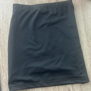 Svart tight kortkjol - Enkel och stilren svart kortkjol med tight passform. Kjolen är rak i modellen och har en elastisk midja för extra komfort. Perfekt att matcha med en crop top eller oversized hoodie.Aldrig använd 