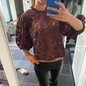 Trekvartsärmad spets blus - Säljer en plommonlila blus med genombruten spets och voluminösa puffärmar. Blusen har rund hals med liten volangkant och knäppning bak i nacken. Den är croppad och har trekvartsärm med resår vid ärmslut. Perfekt för dig som gillar romantiska detaljer. Från newbie