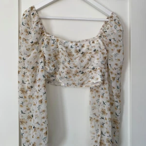 Blommig blus med puffärmar från Boohoo - Supersöt blommig cropped blus från Boohoo i vitt med gula och gröna detaljer. I storlek 36. Använd ett fåtal gånger. 