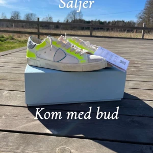 Phillipe model neongula detaljer - Säljer ett par vita sneakers med neongula detaljer och grå häl. Skorna har snörning och en rund tå. Perfekta för en trendig look. Köpta för 3900 